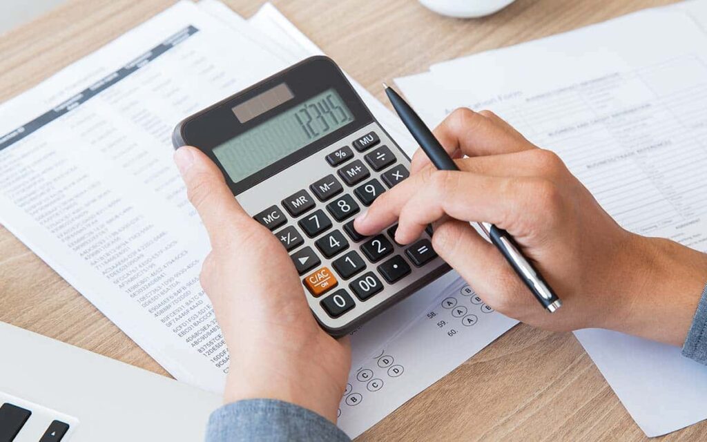 Homem mexendo em uma calculadora representando custos e despesas